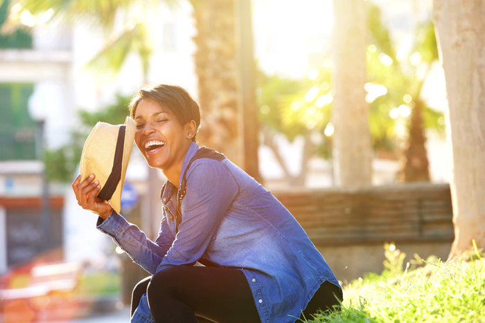 women laugh into her hat while sitting on grass