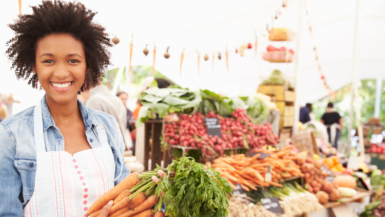 African American woman at a farmers market holding carrots during the day