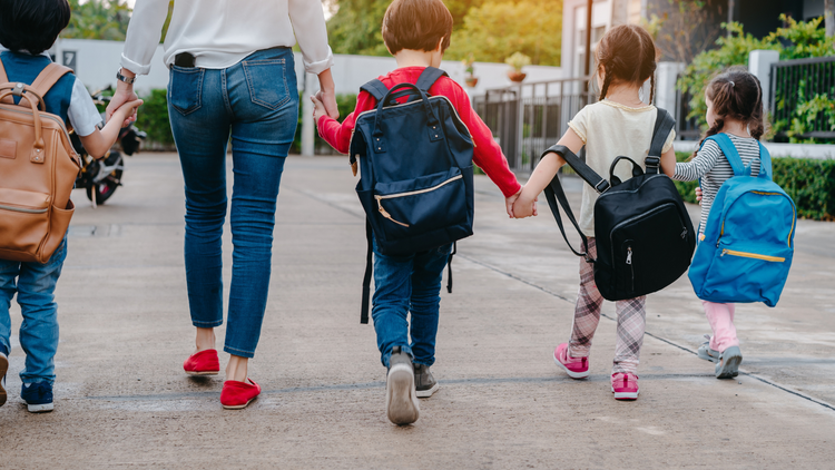 A mother and her four kids who are back-to-school ready. All the kids are wearing backpacks that are too big for them. 