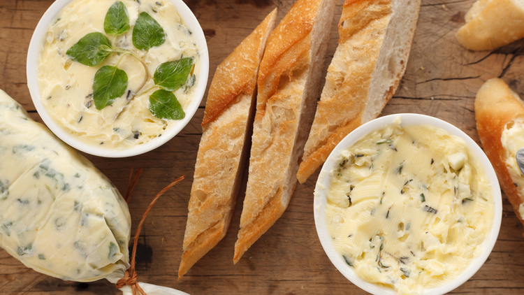 An image of a cutting board with a sliced baguette and a couple bowls of Cowboy Butter. There is also a log of Cowboy Butter.