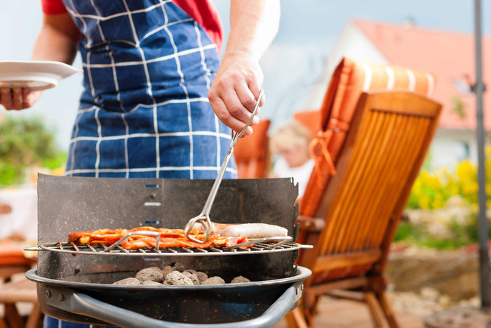 man cooks chicken over a charcoal girl on a summer day