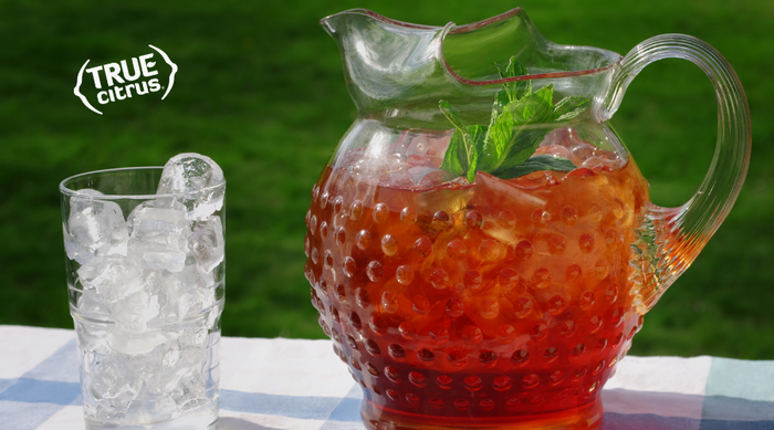 Pitcher of spiked Arnold Palmer and empty glass of ice on a picnic table outside in the summer.