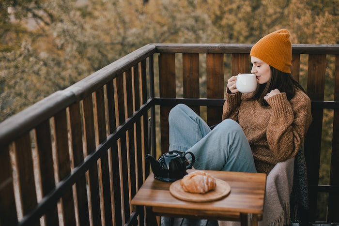 Woman sipping a fall drink out of her mug during autumn, she is sitting outside on her porch admiring the nature