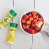 A little kid reaches for a large bowl of fresh strawberries and watermelon, which are lightly dashed with True Lemon. A True Lemon Shaker and True Lime Shaker rest on the table next to the bowl.