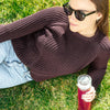 A woman lounging in the grass enjoys a bottle filled with True Lemon Energy Blueberry Acai. 