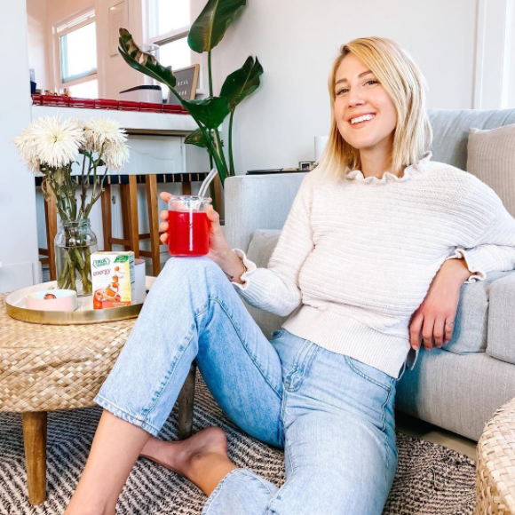 A woman happily sits in her stylish living room and enjoys a glass of True Lemon Energy Strawberry Dragonfruit. 