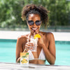 A woman in the pool wearing sunglasses smiles and takes a sip of water flavored with True Grapefruit.